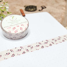 Load image into Gallery viewer, A roll of Berries washi tape in its packaging sits on a bullet journal page. Below that is a strip of tape along the page. The pattern features delicate berry twigs resembling holly leaves. There are some botanicals and an old pocketwatch and key in the background.
