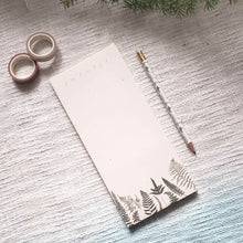 Load image into Gallery viewer, A styled photo of the June &amp; December brand Daily To Do Fern Notepad on a boho beige and blue throw blanket. There is a pencil with fern designs on it beside the notepad as well as two rolls of neutral colored washi tapes and a hint of a real fern peeking into the photo
